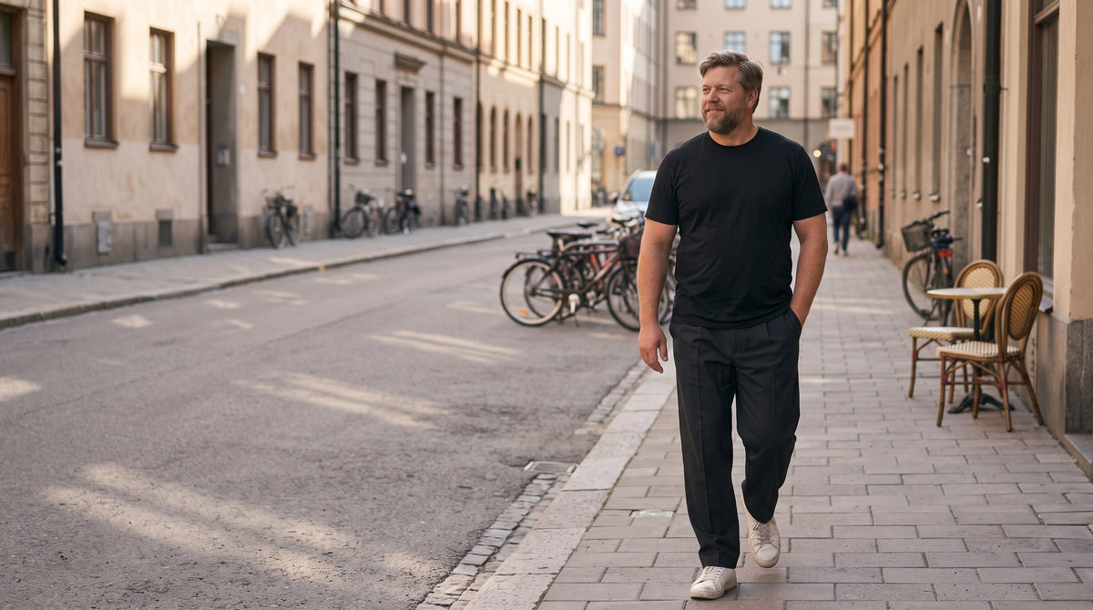 Man i svart t-shirt och mörka kostymbyxor promenerar på en gata i Stockholm en höstmorgon