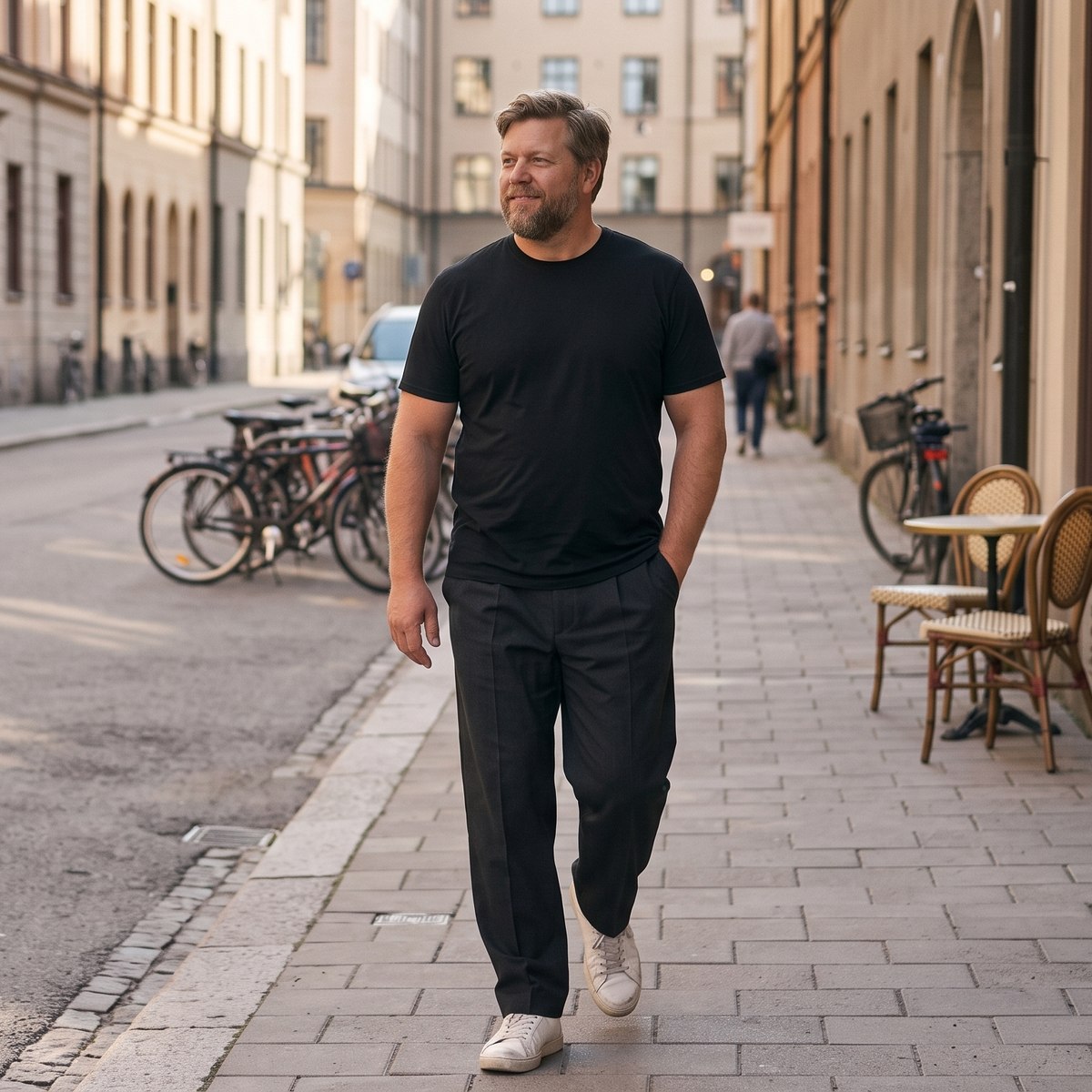 Man i svart t-shirt och mörka kostymbyxor promenerar på en gata i Stockholm en höstmorgon